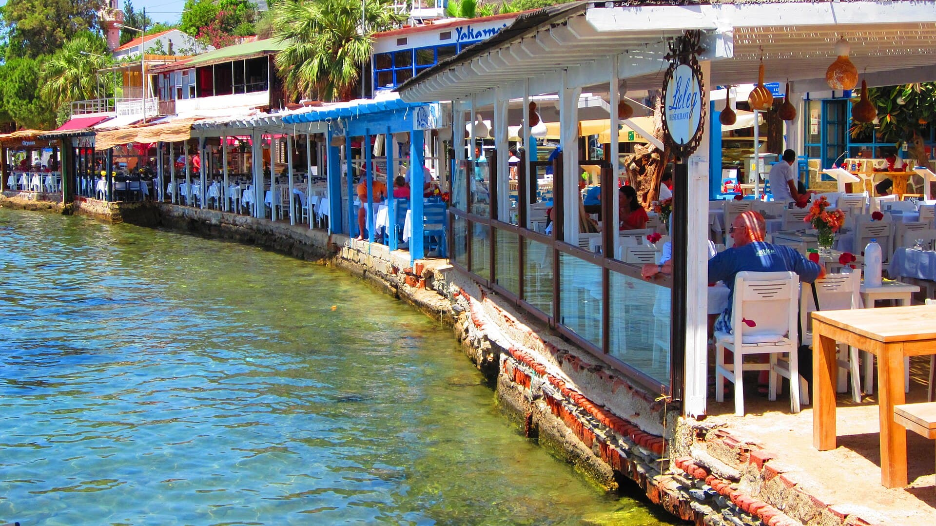 Fishing boats moored along Gümüşlük's sunlit waterfront near Bodrum, Türkiye.