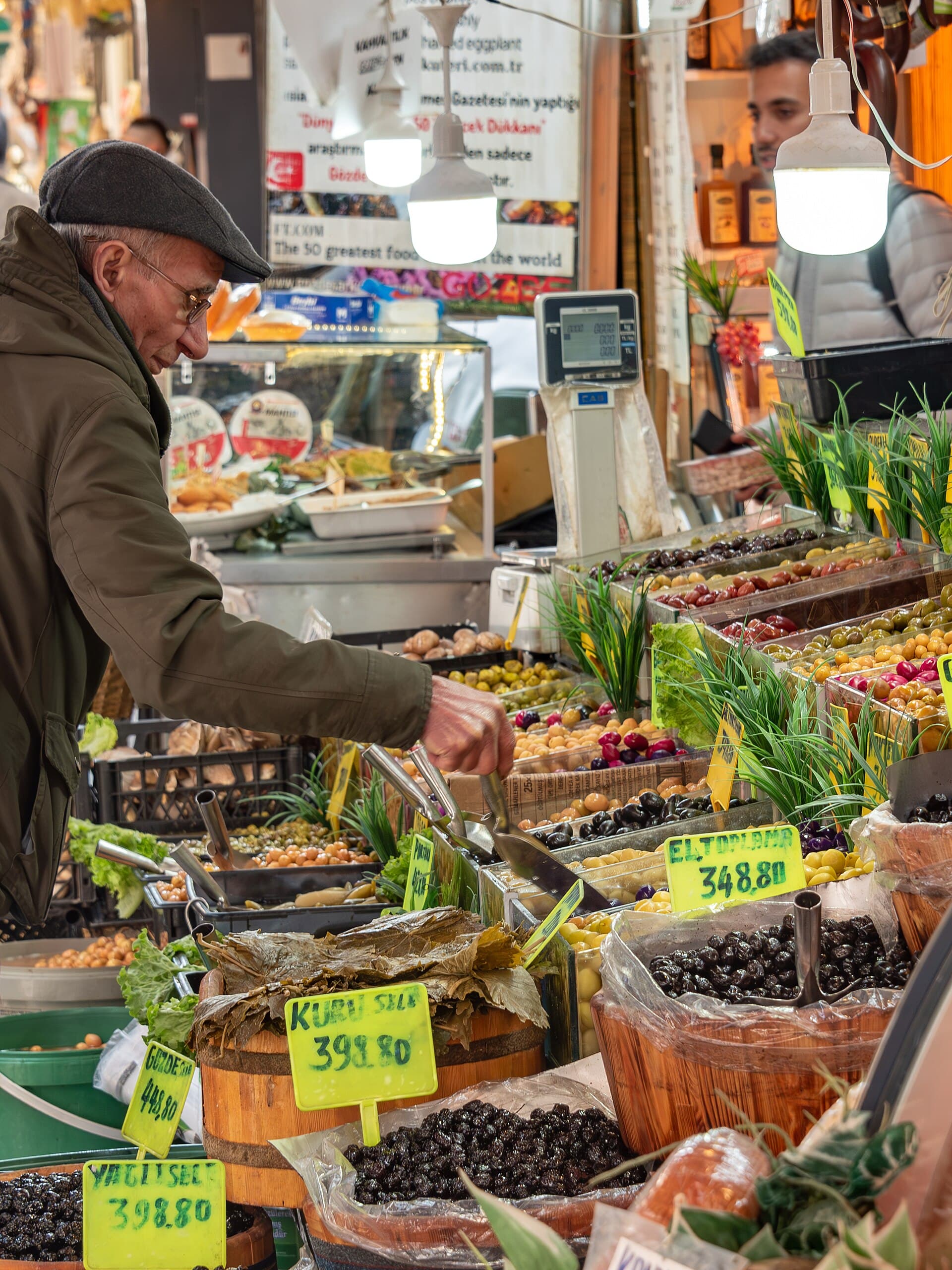 A vendor arranges olives and pickled vegetables at a market stall in the Kadıköy çarşı