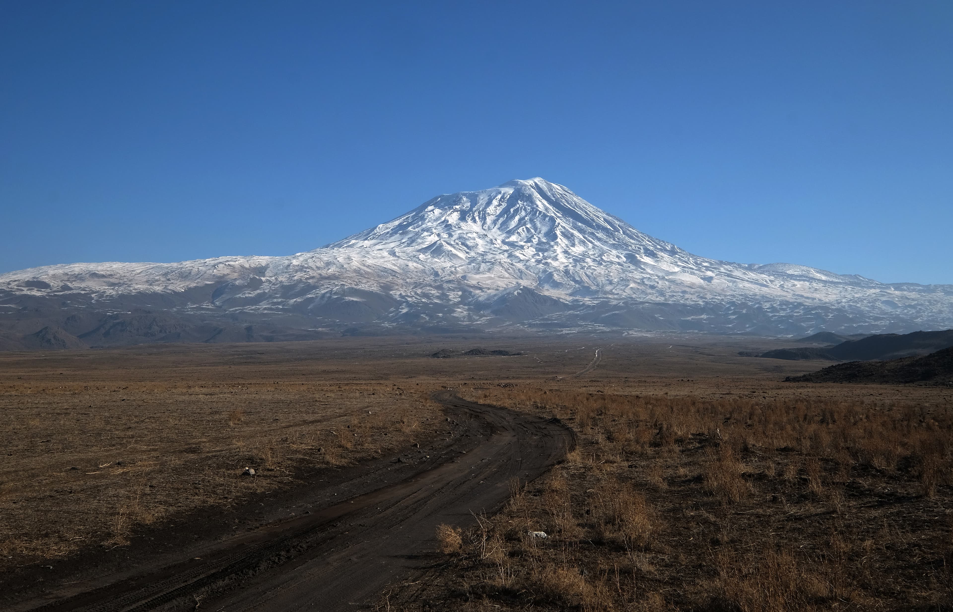 Snow-covered Mount Ararat's summit rising above a dirt road and open steppe