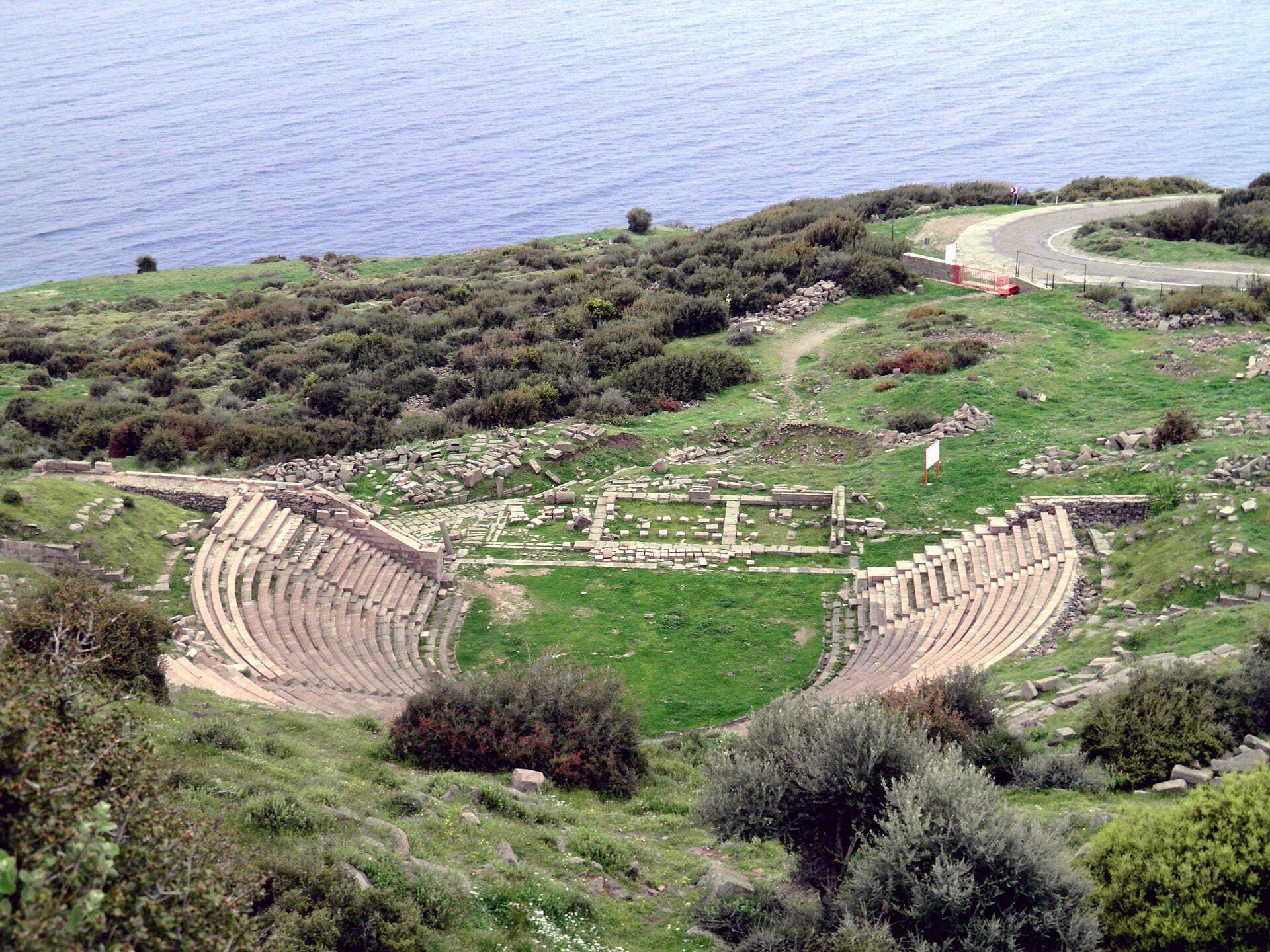 Elevated view of the ancient theatre at Assos with the Aegean Sea behind the seating tiers.