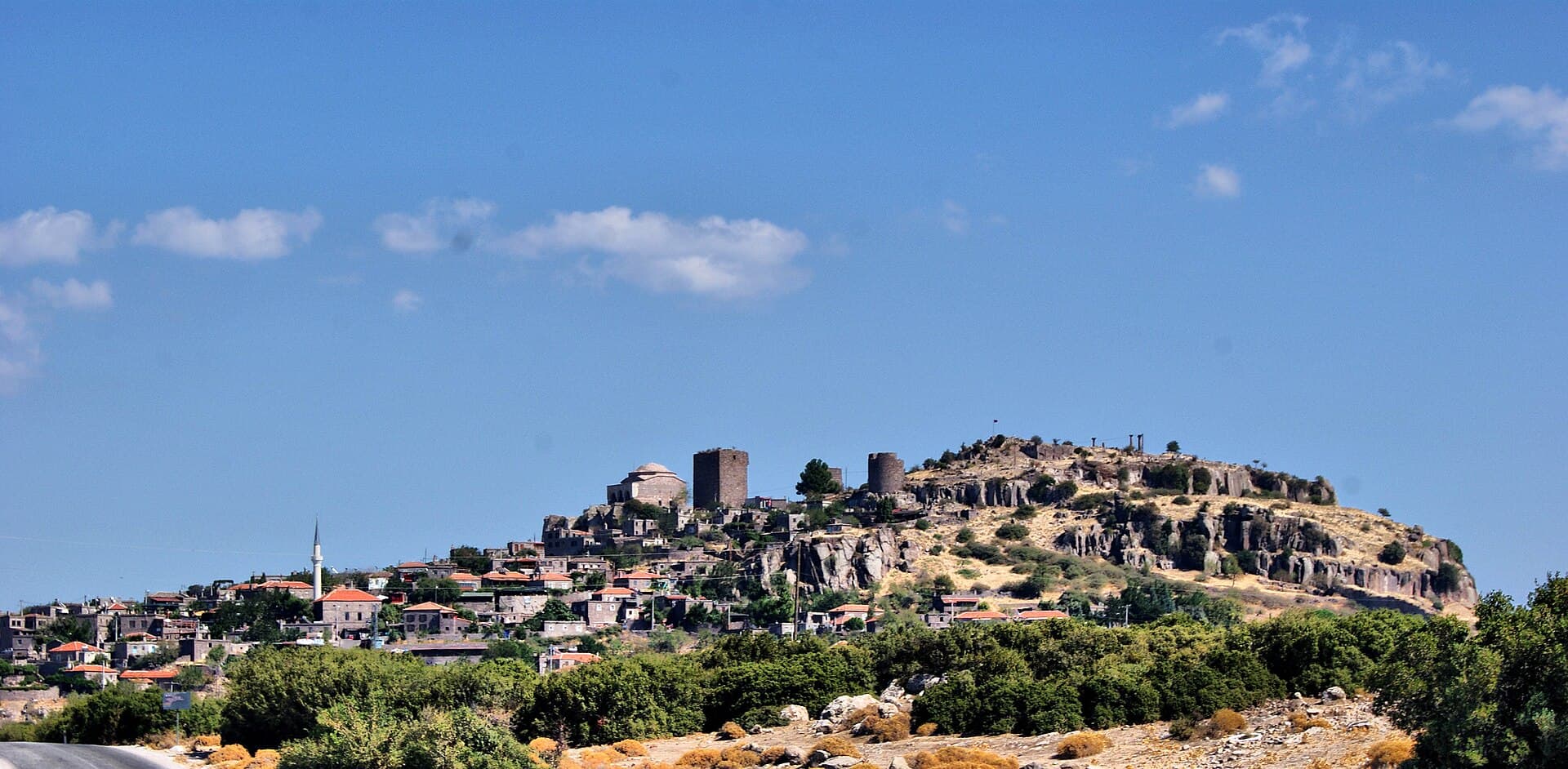 Wide daytime view of Behramkale village with the Assos acropolis crag above it.