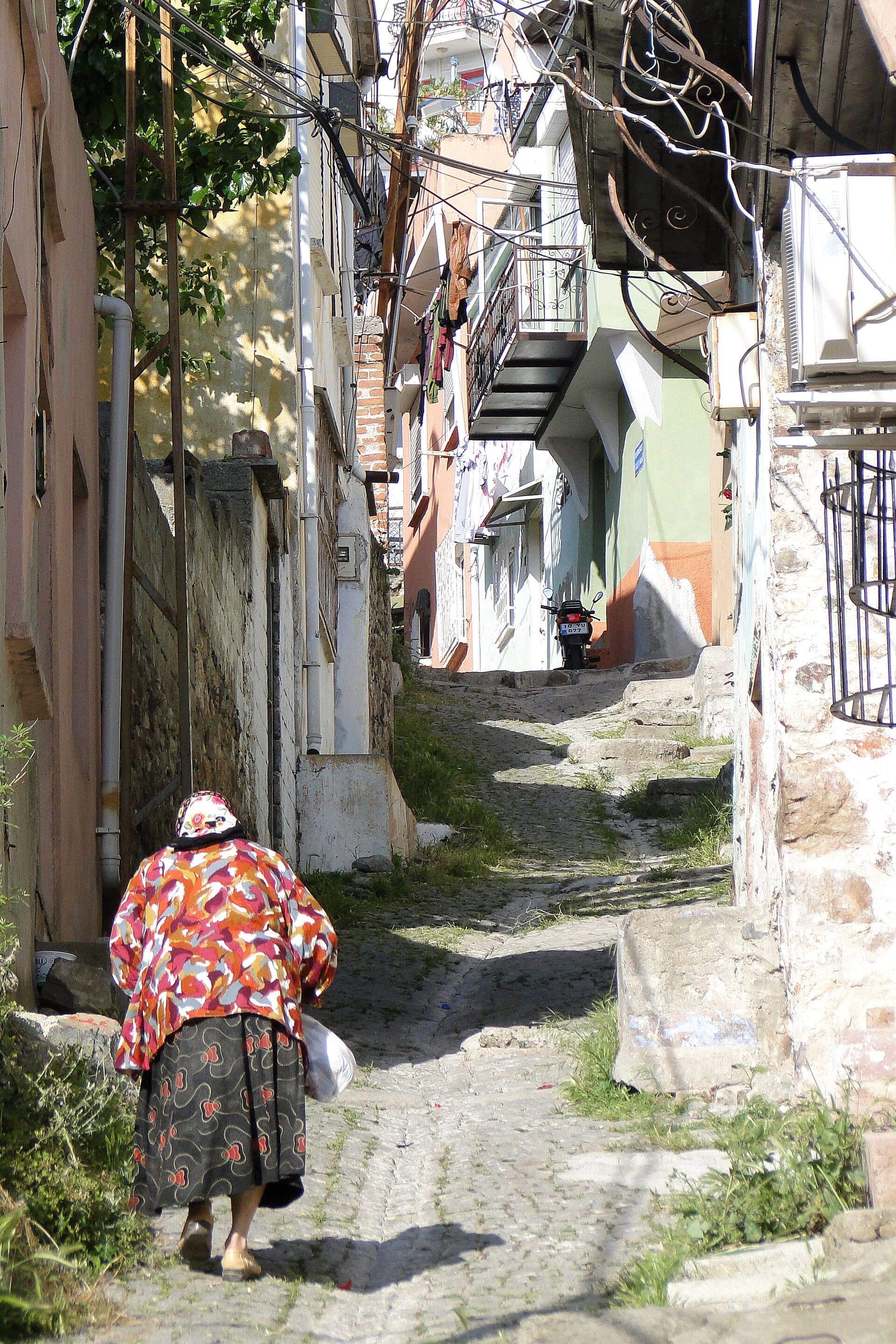 Sunlit cobbled street lined with historic stone houses in Ayvalık's old town.