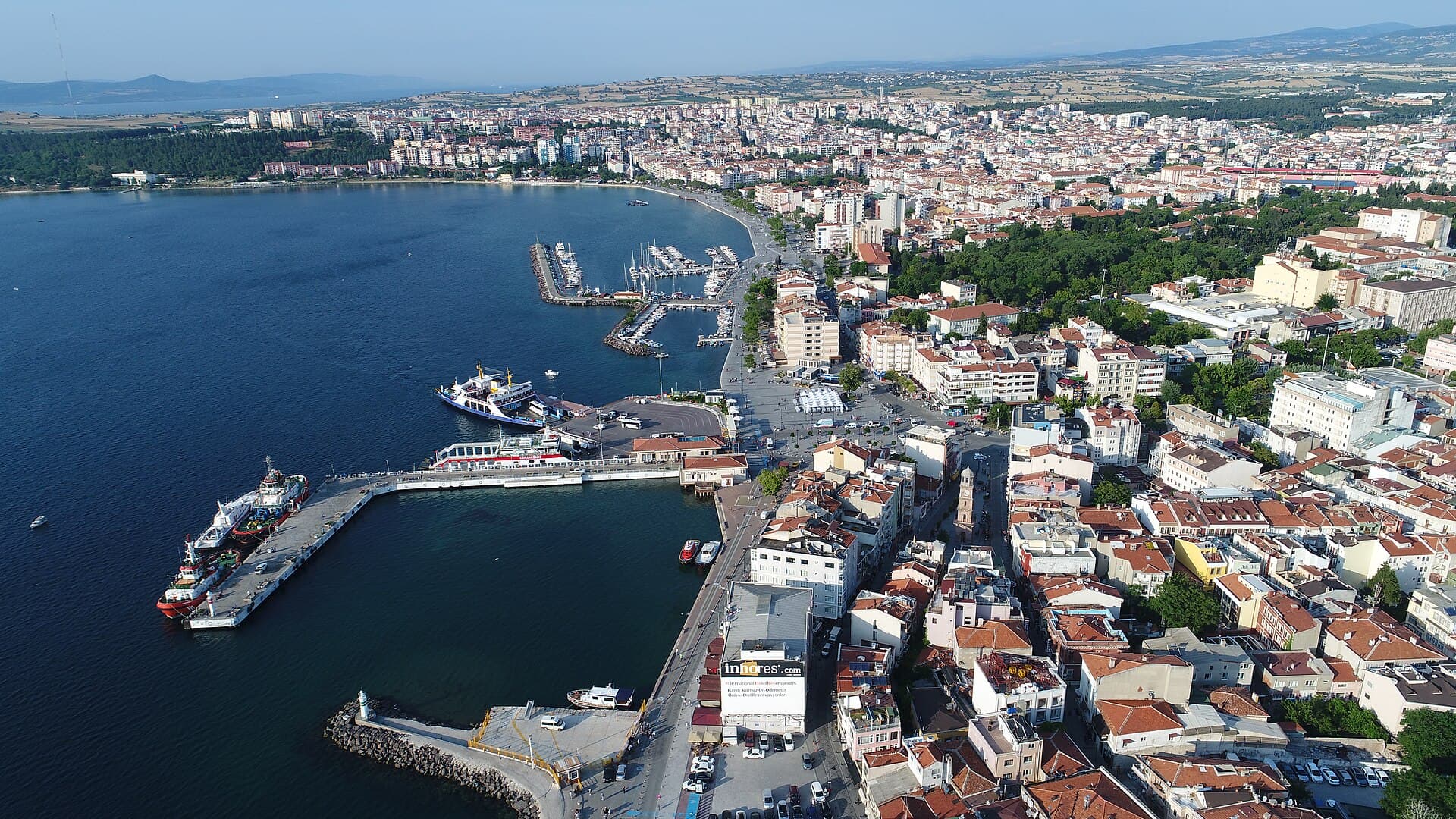 Aerial view of Çanakkale's curving harbor promenade, marina, and a docked ferry