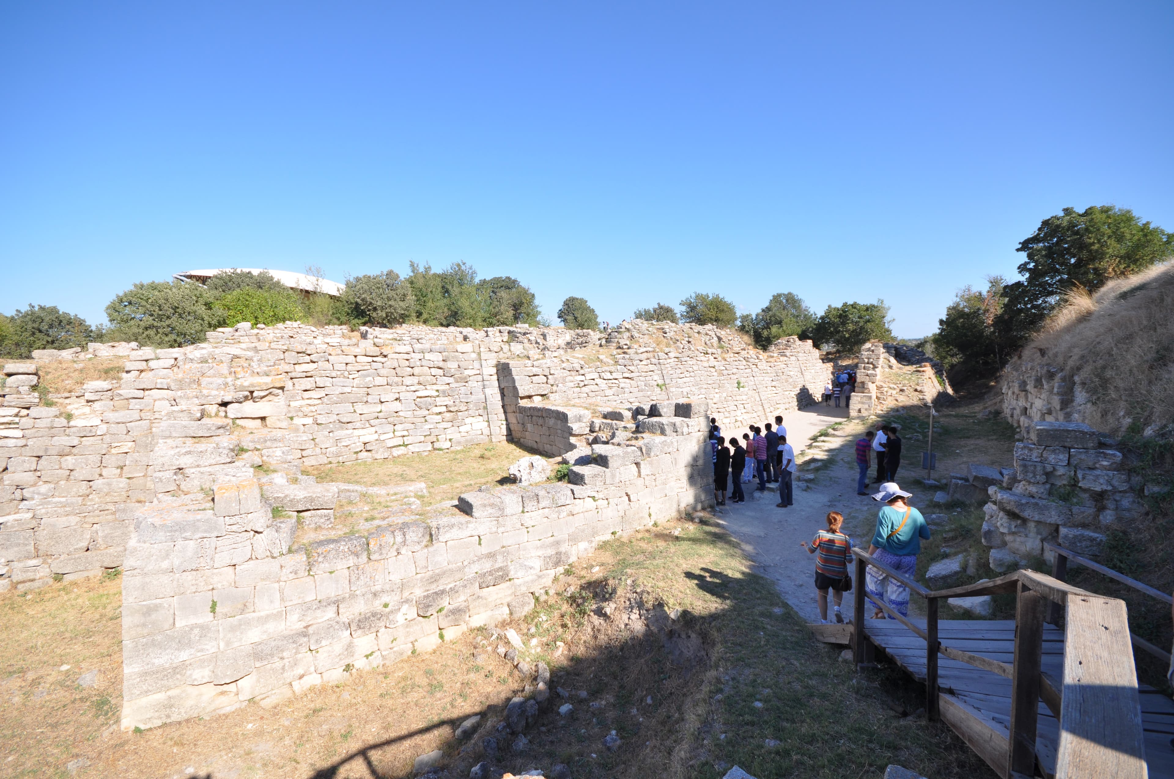 Sloped, offset stone blocks of Troy's ancient fortification wall, tourists walking alongside
