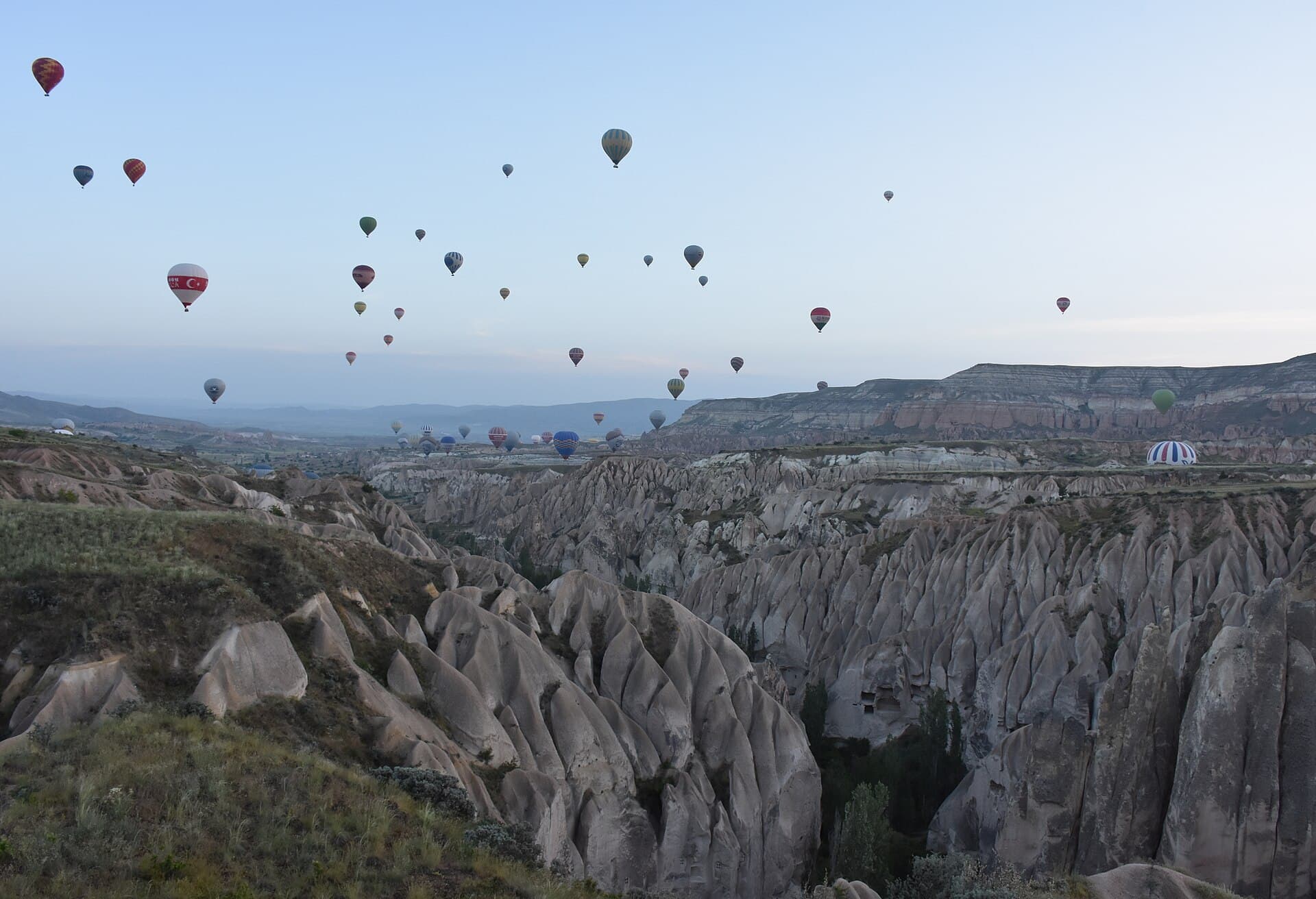 Dozens of hot air balloons fill the sky at dawn above the fairy-chimney valleys near Göreme, Cappadocia
