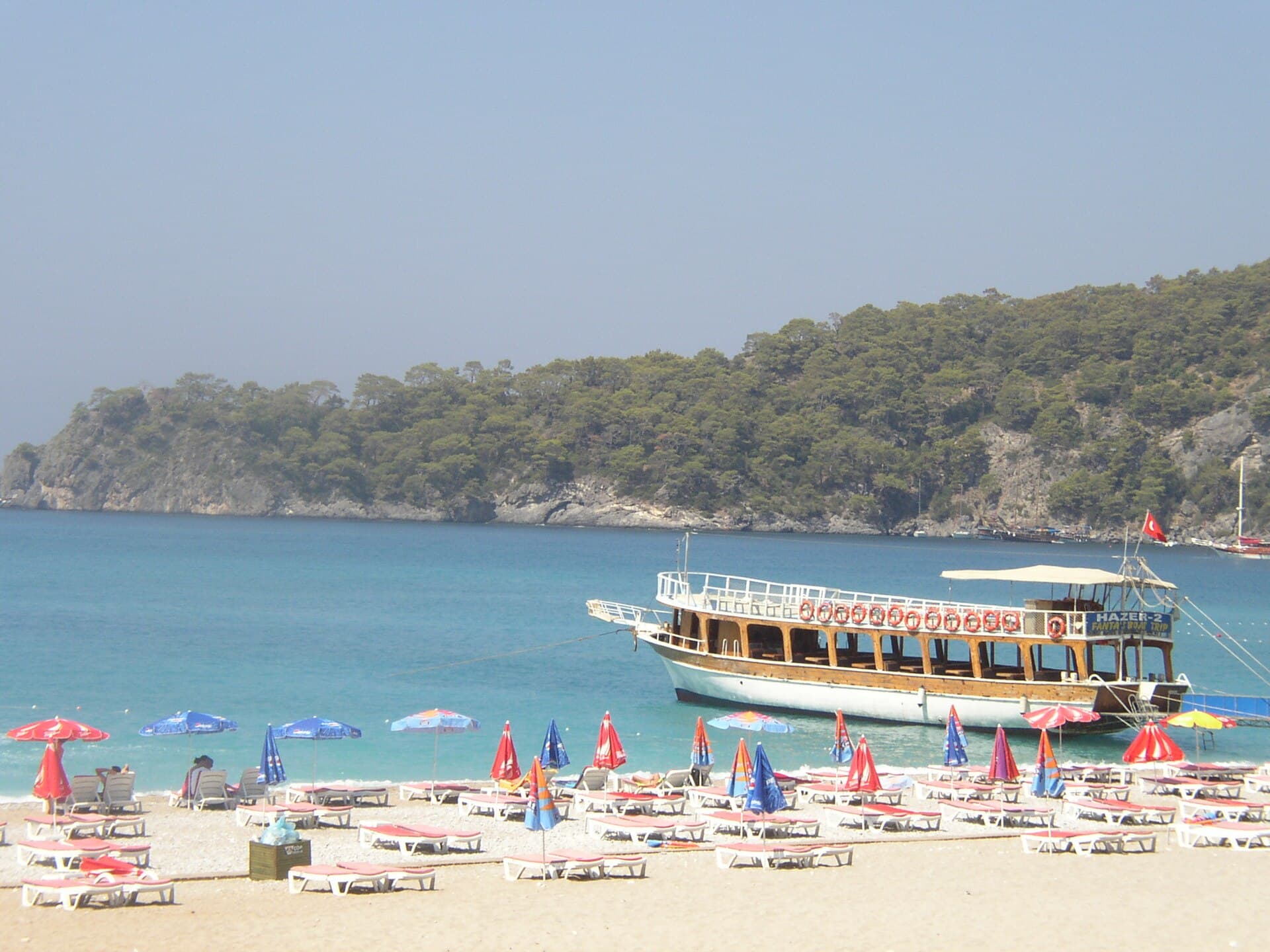 Sunbeds and a tour boat along the turquoise shoreline at Ölüdeniz beach.
