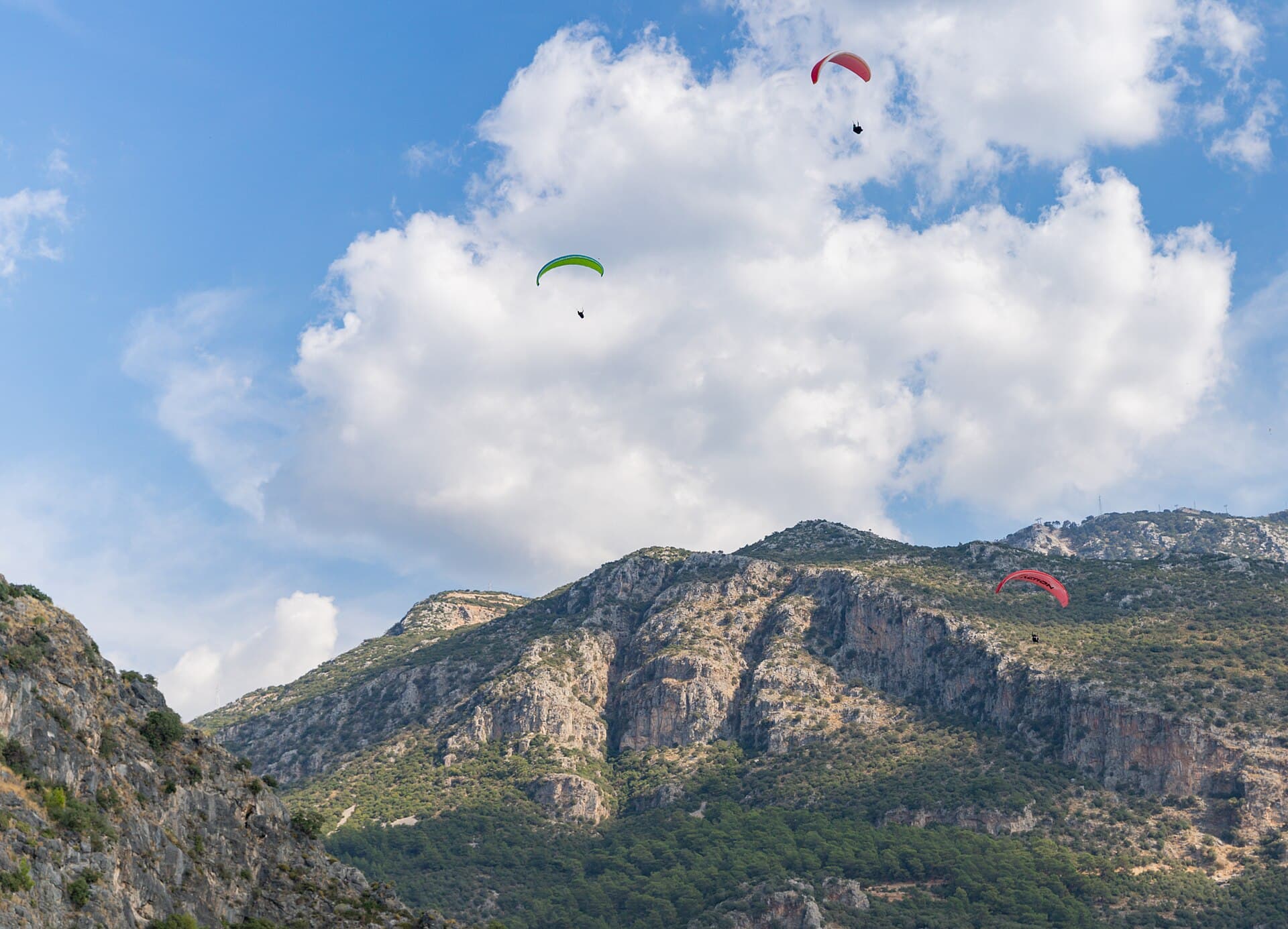 Colorful paragliders drift above Babadağ's cliffs over Ölüdeniz, Türkiye.
