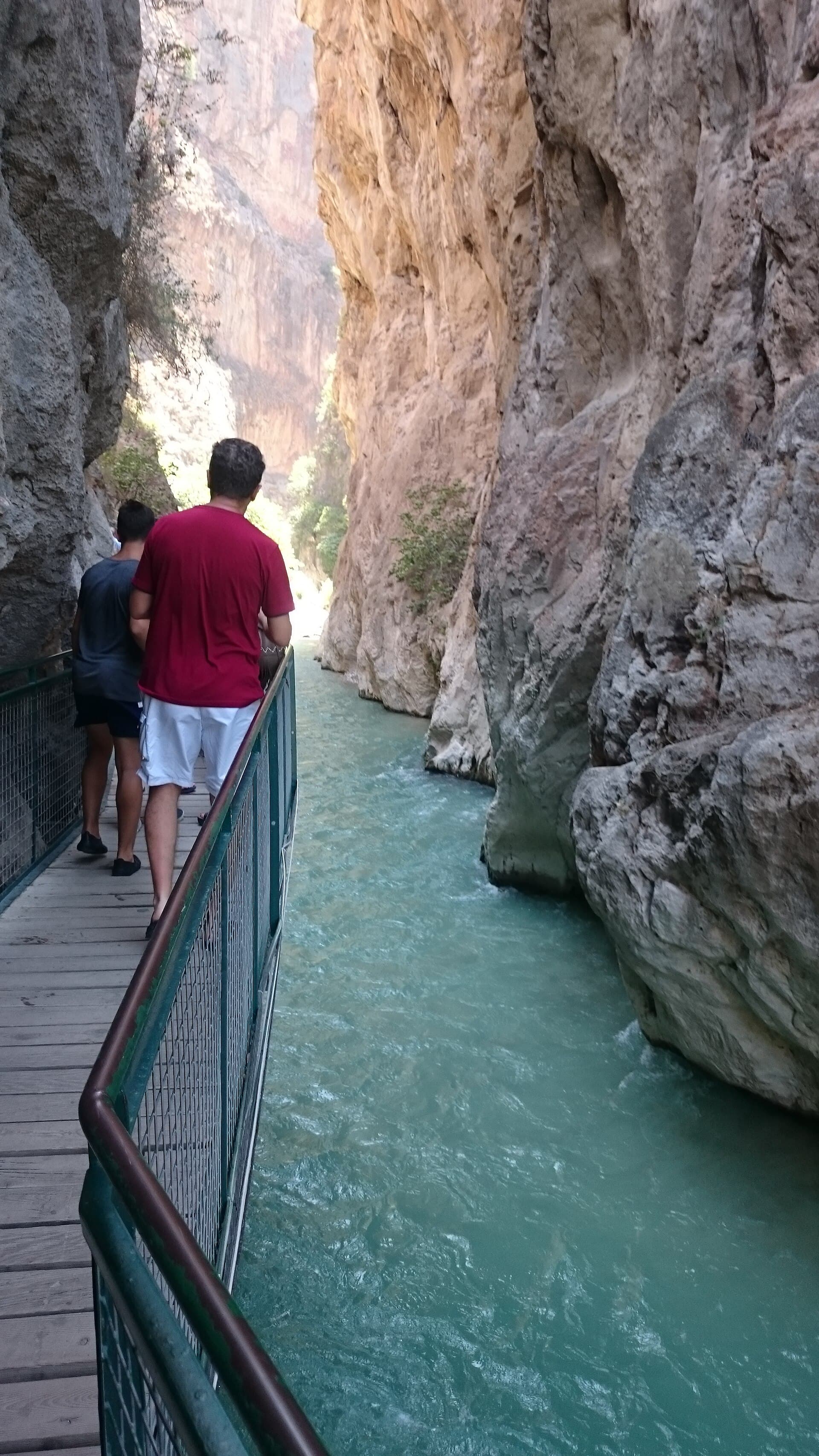 Wooden walkway with railing clings to the gorge wall above turquoise meltwater.
