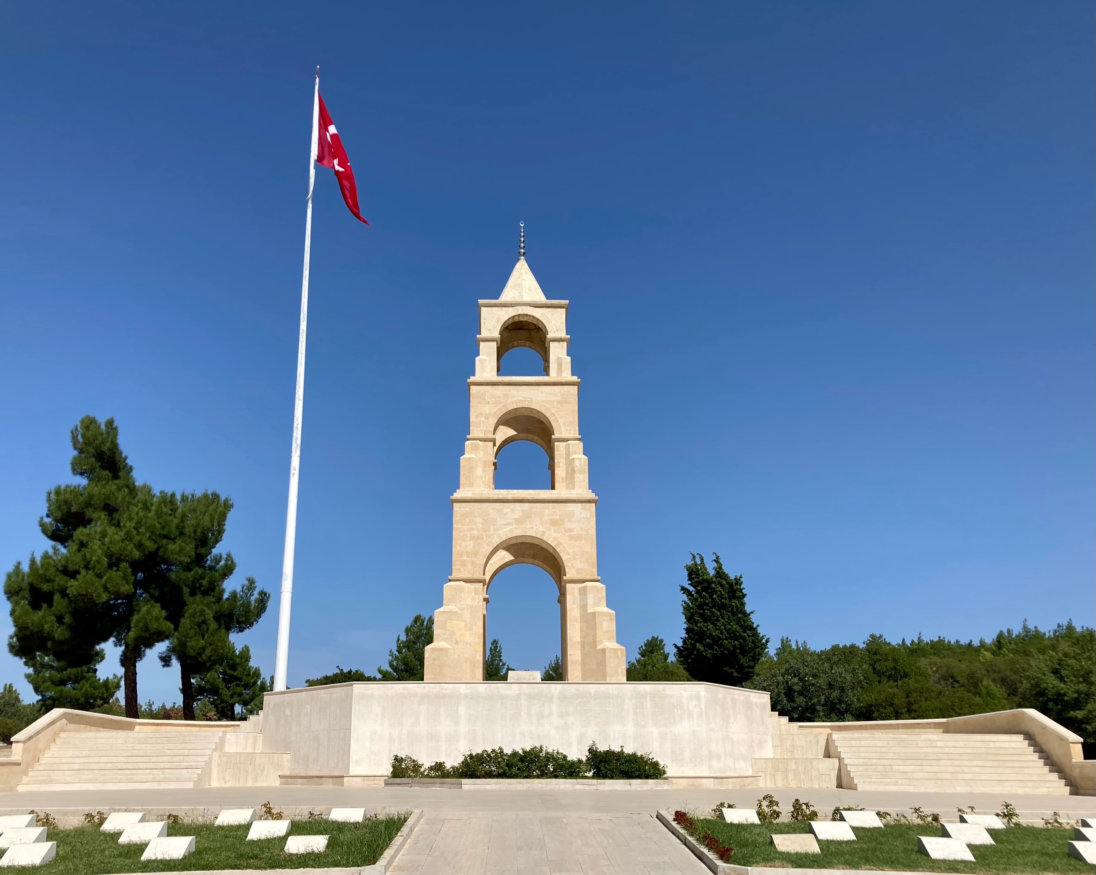 Limestone memorial tower topped with a Turkish flag against a clear blue sky