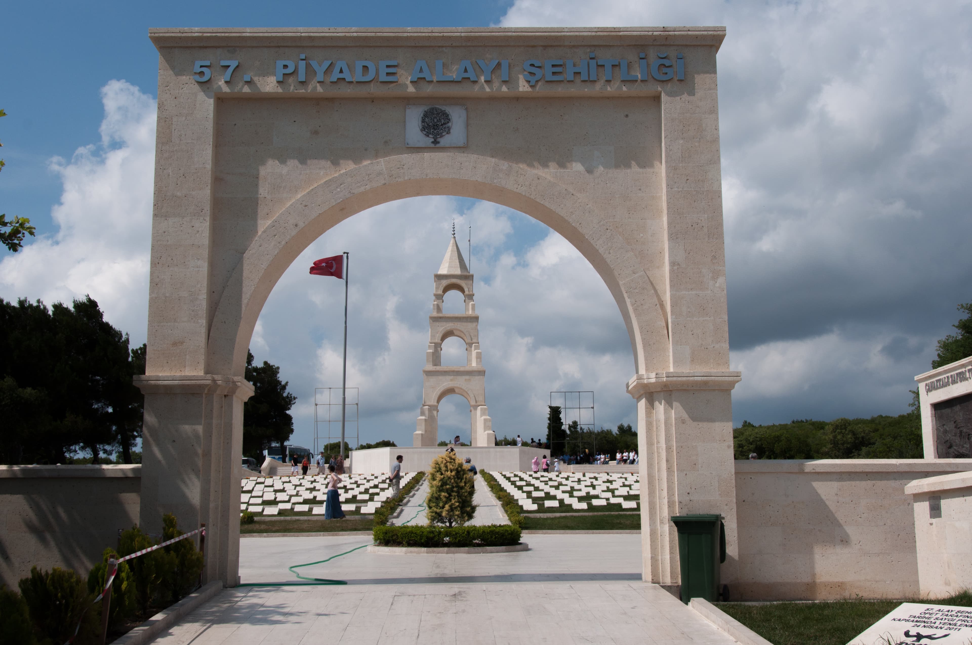 Stone archway reading "57th Infantry Regiment Cemetery," with the memorial tower and headstones behind