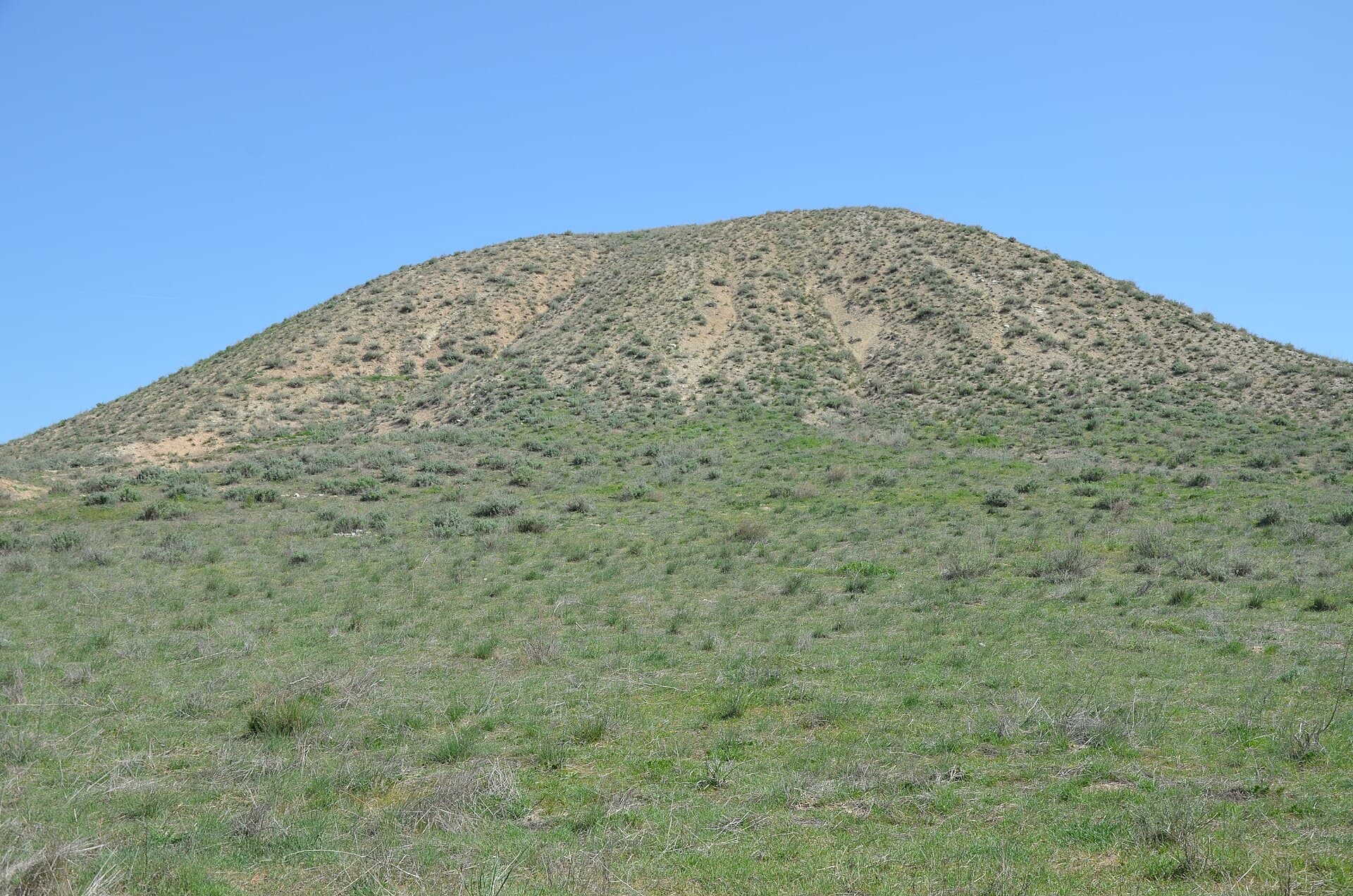 Grass-covered Midas Mound tumulus rising against a clear blue sky.