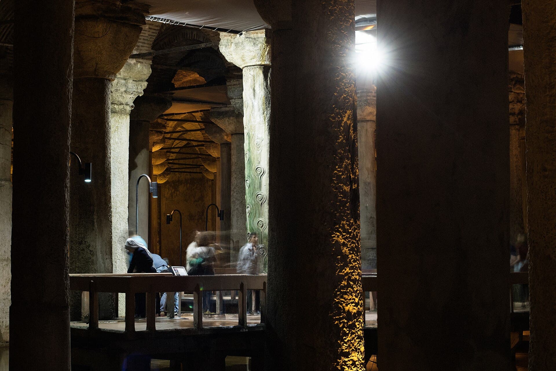 Rows of ancient stone columns inside the Basilica Cistern, dramatically lit with visitors crossing a wooden walkway