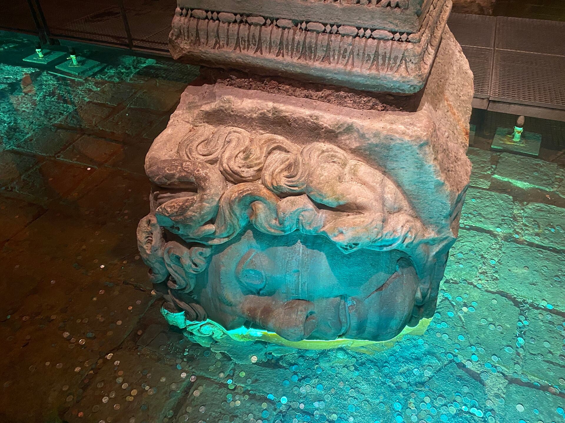 Sideways-facing carved Medusa head used as a column base in the Basilica Cistern, partly submerged in illuminated water