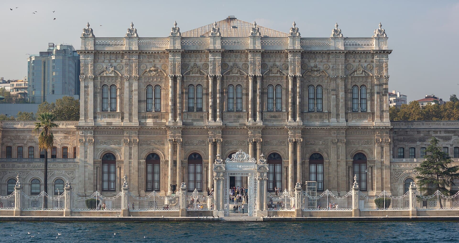 Dolmabahçe Palace's ornate white facade and waterfront gate viewed from across the Bosphorus