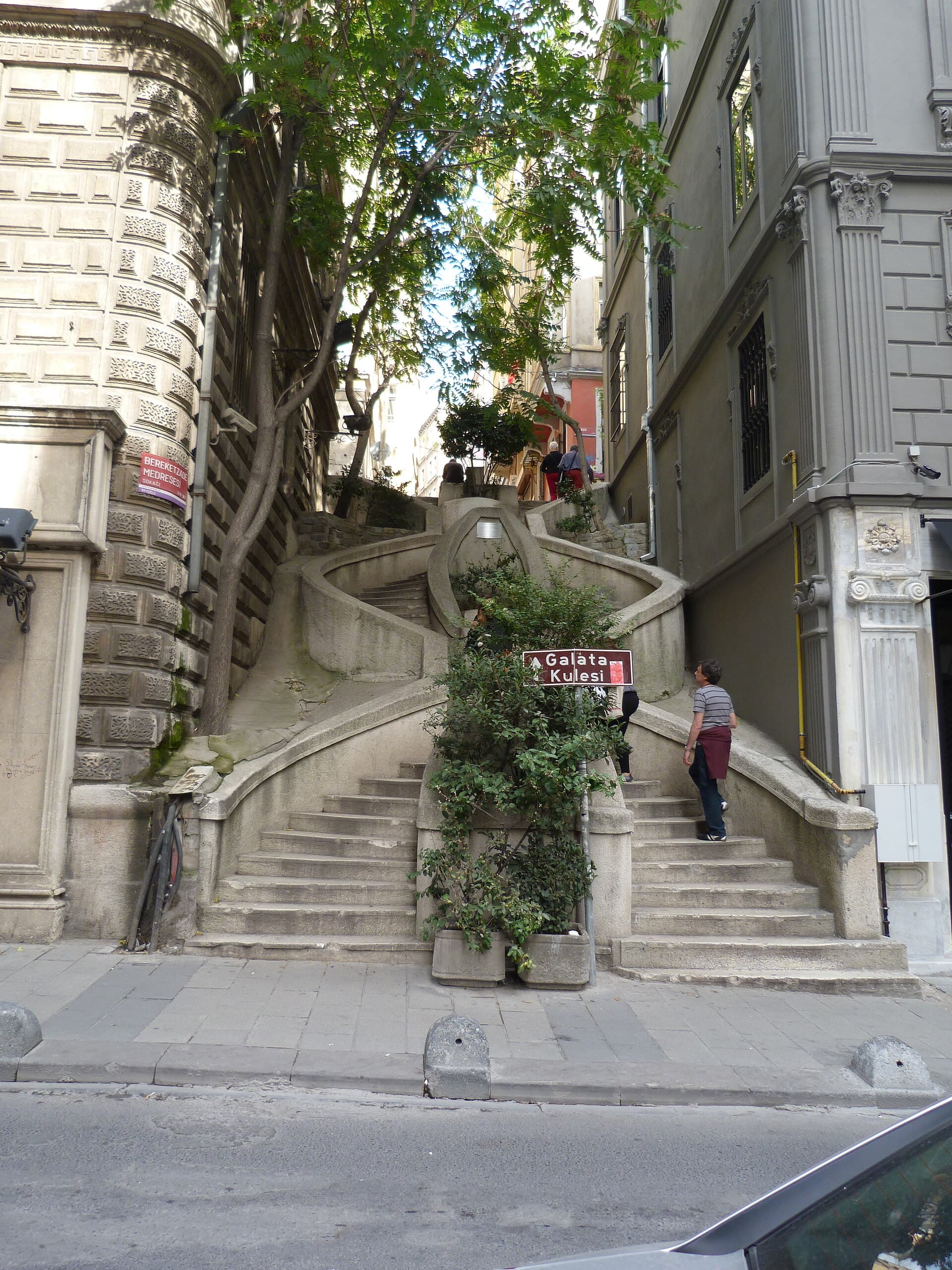 Pedestrians climb the curving Kamondo Steps in Galata, shaded by trees between old apartment buildings