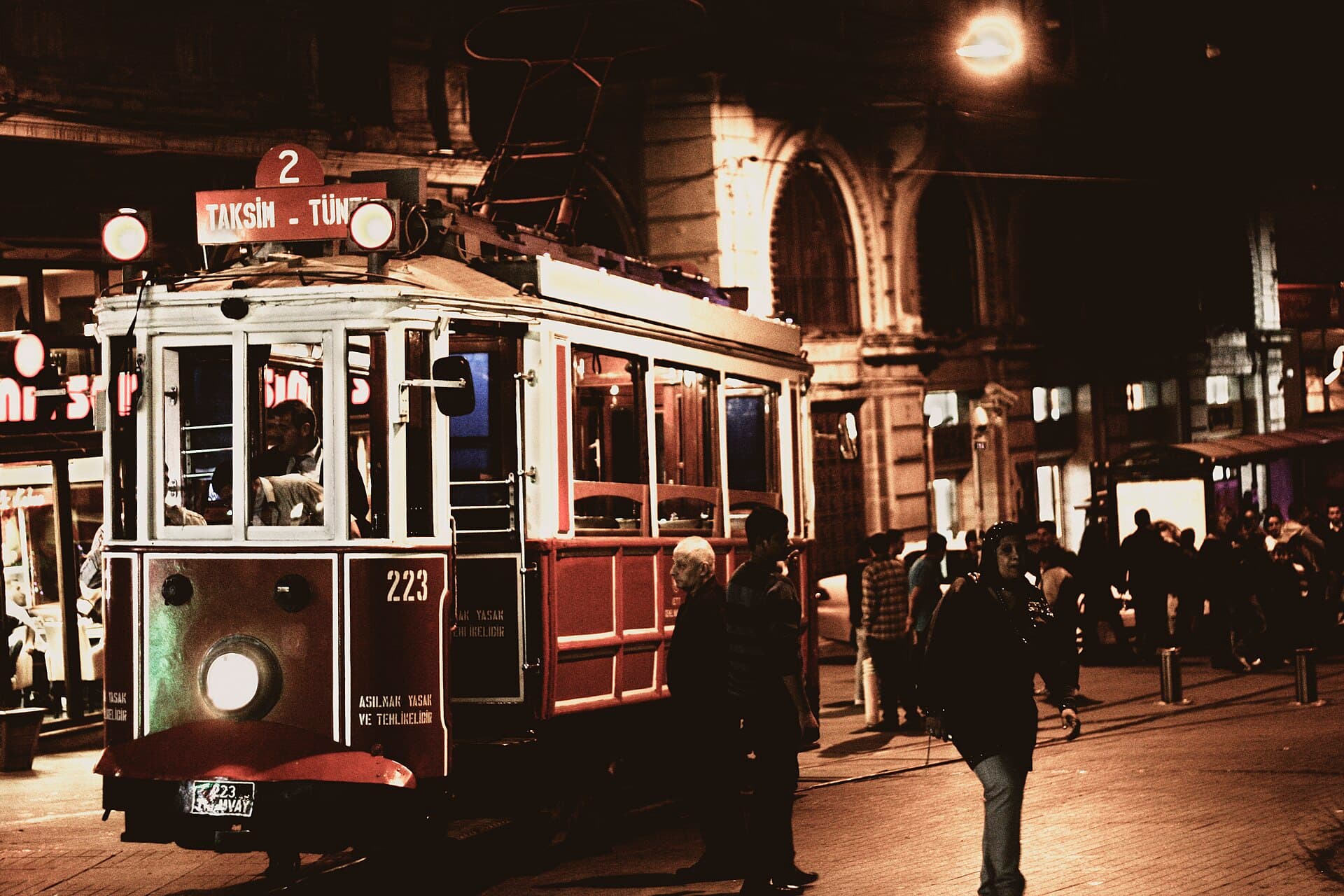 Historic red tram on the Taksim-Tünel route running along İstiklal Avenue at night, with pedestrians strolling the pavement