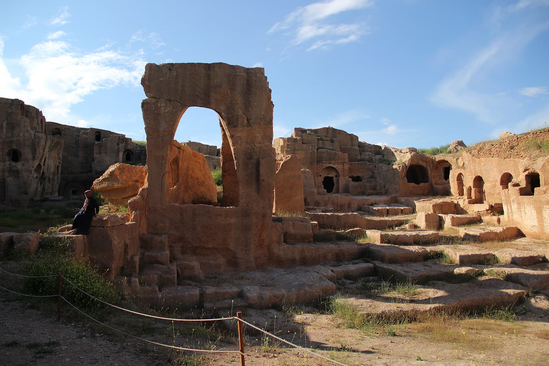 Sunlit rock-cut tomb galleries and ruined archway at Dara's ancient necropolis.