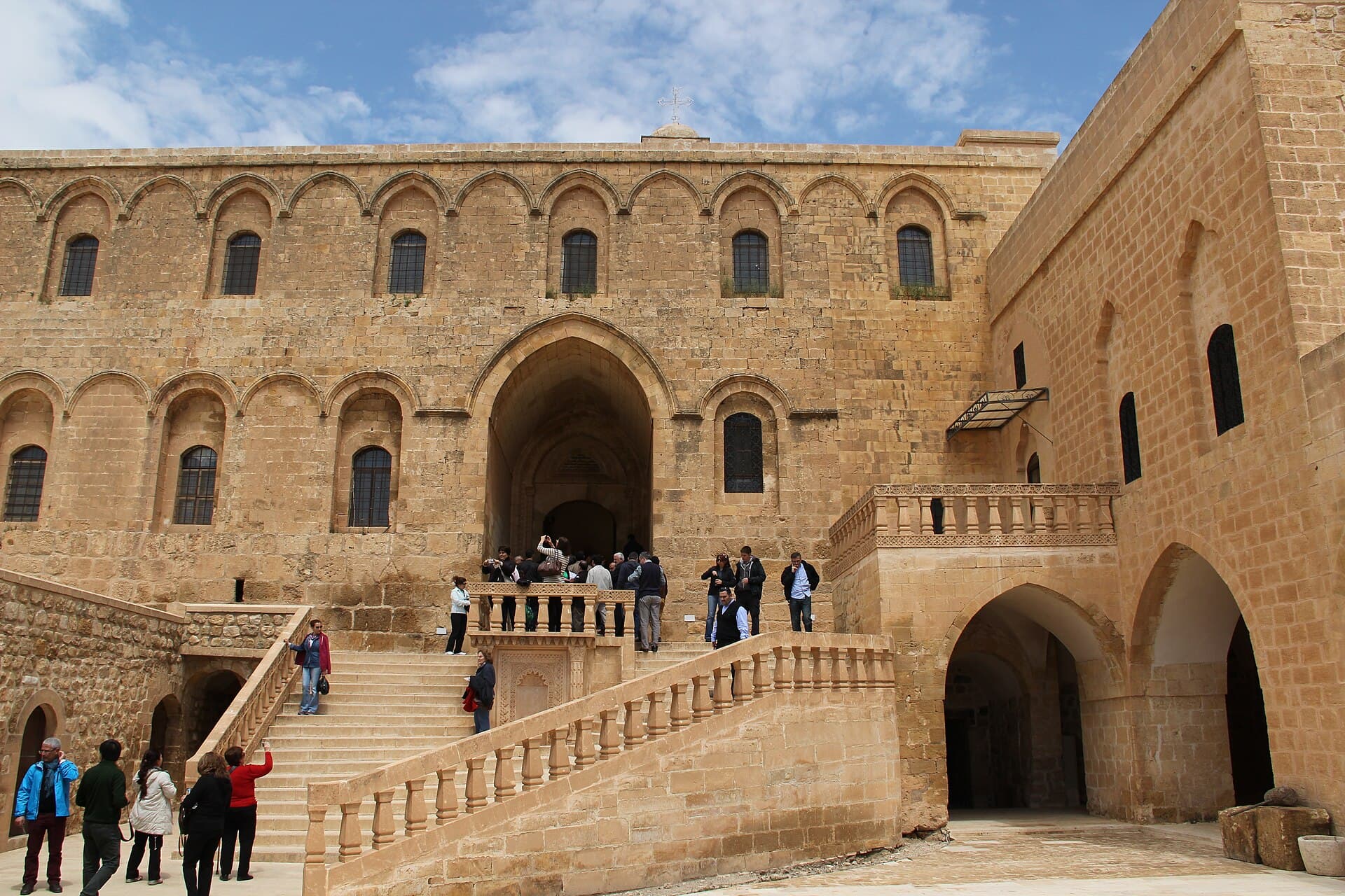 Visitors climb the grand staircase toward Deyrulzafaran Monastery's honey-stone church entrance.