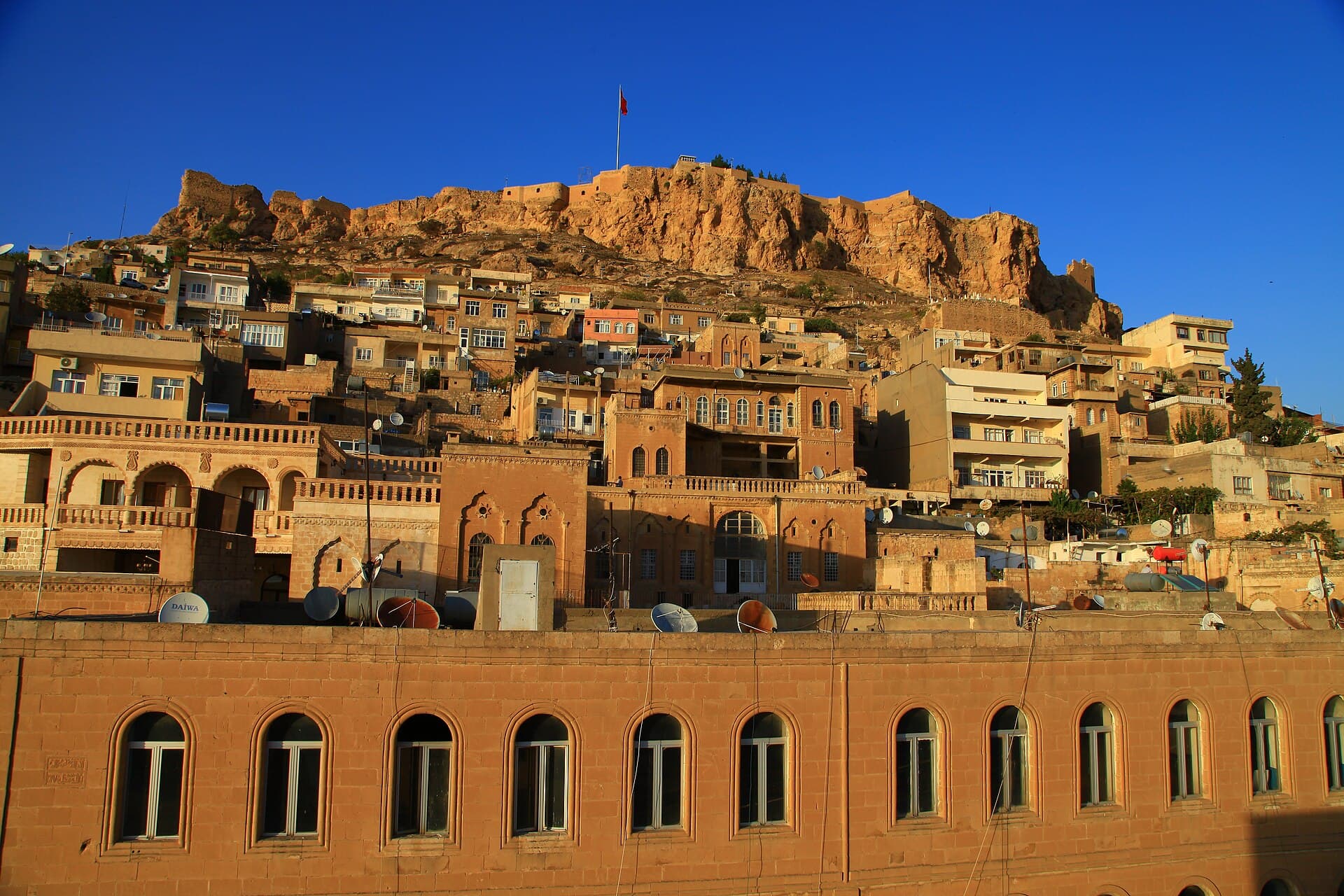 Mardin Castle crowns the old city's golden stone rooftops in warm sunlight.