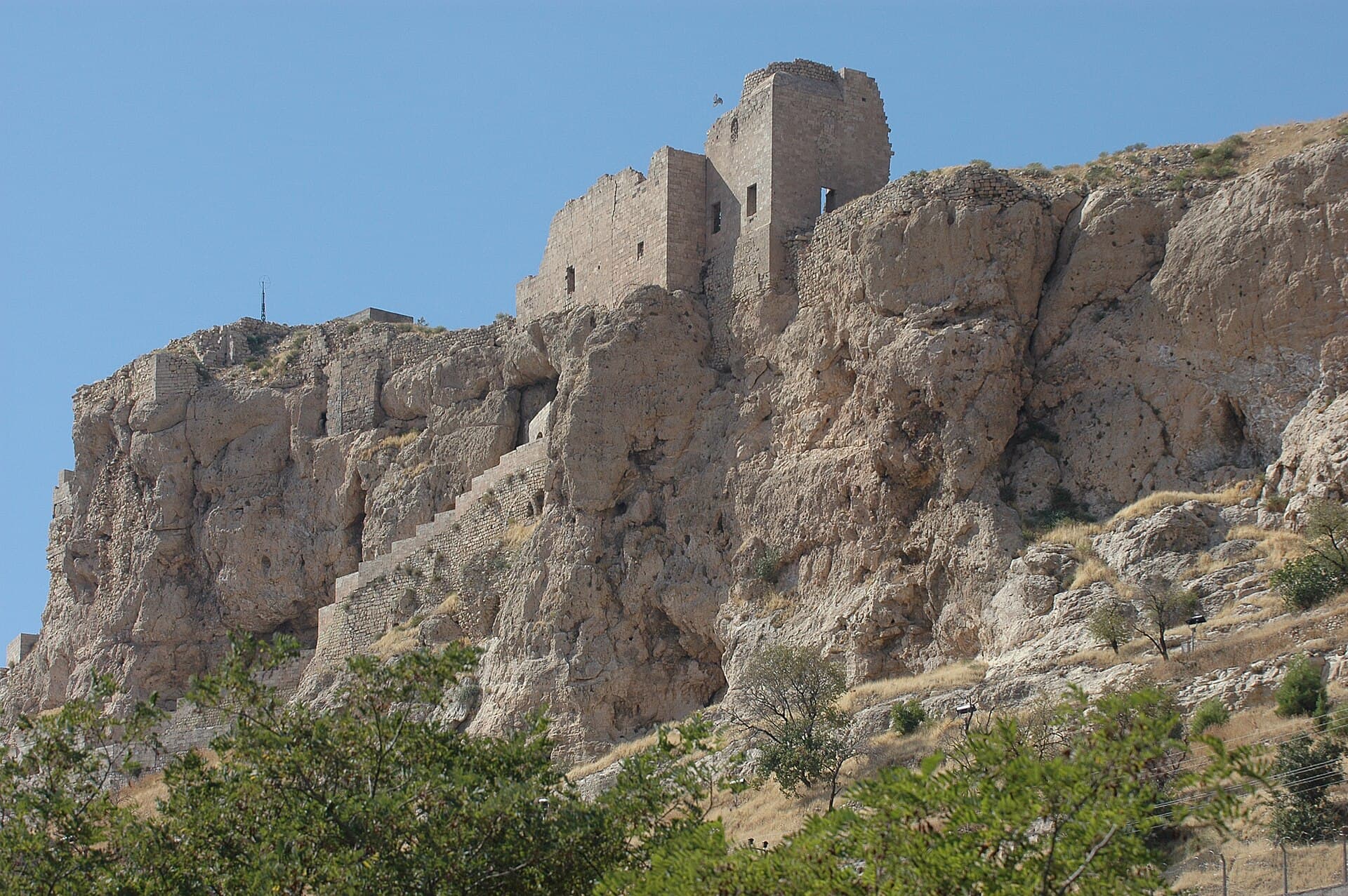 Weathered stone towers of Mardin Castle perched atop a rocky cliff.