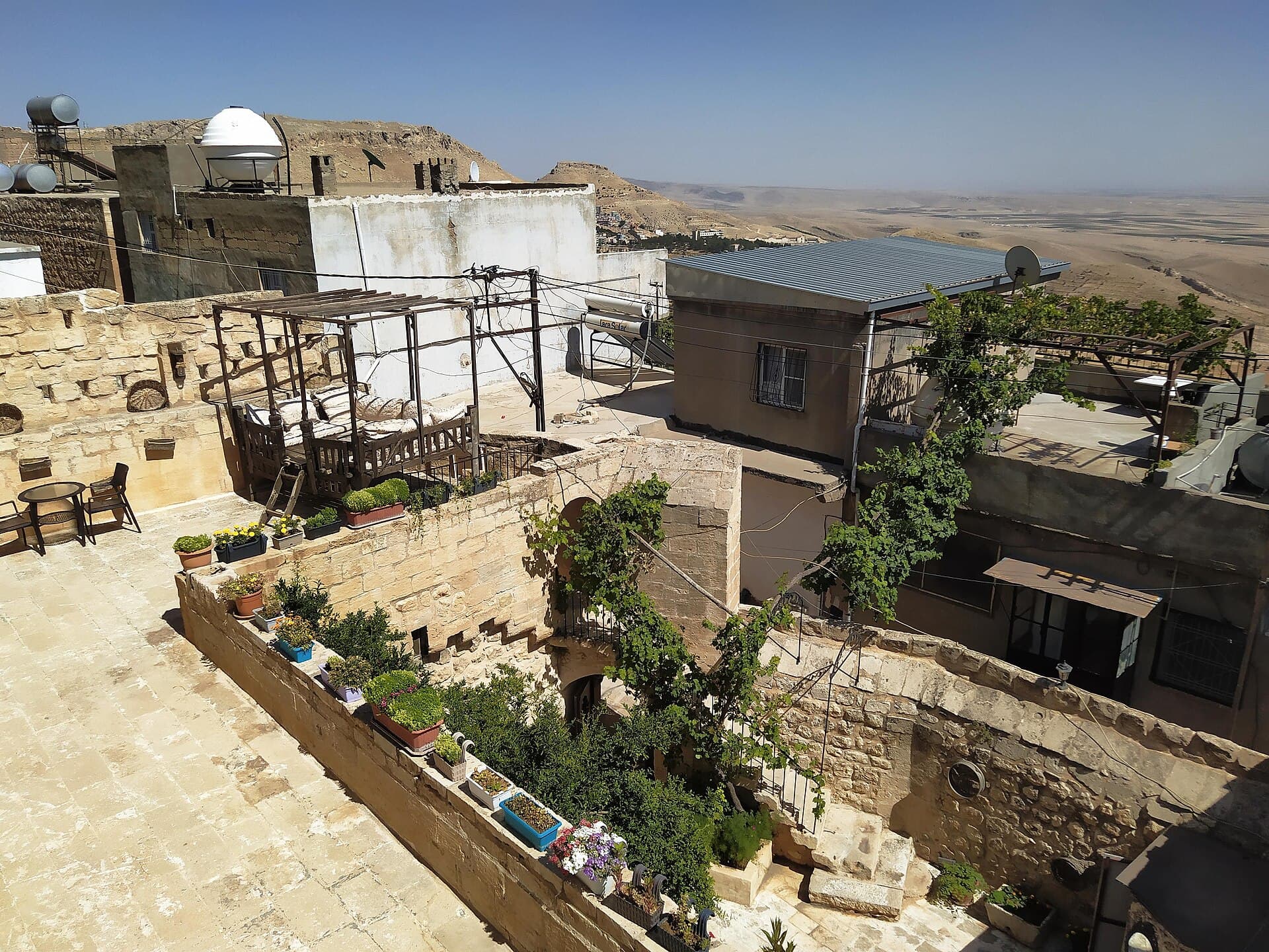 Sunlit honey-stone rooftop terrace in old Mardin overlooking the hazy plain.