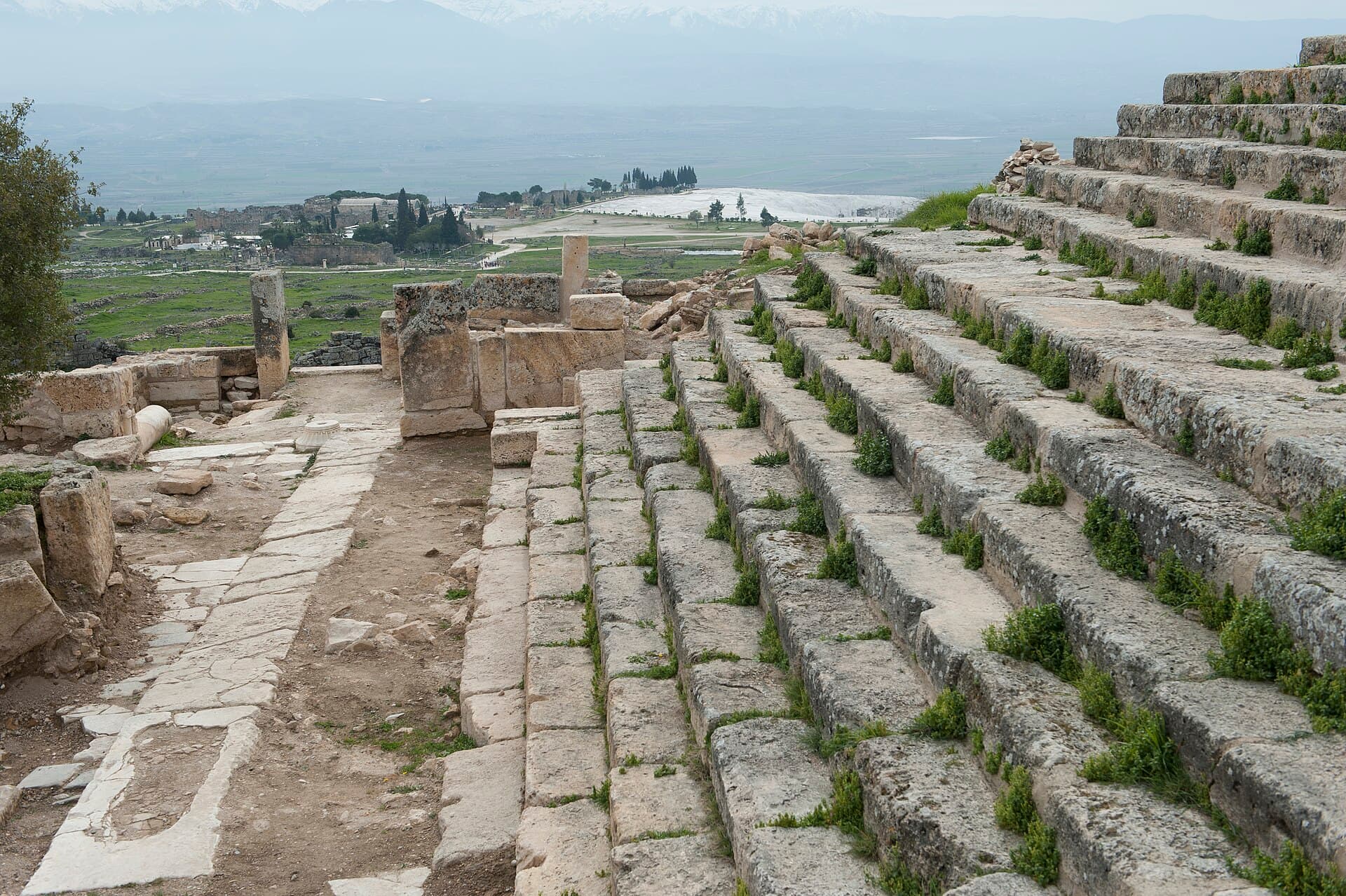 The broad stone processional staircase of the Martyrium of St Philip descends the hillside, with the ruins of Hierapolis and the white travertine terraces of Pamukkale visible on the plain below.